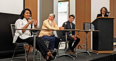 Horizontal photo of Zakiya Whatley speaking, seated along side Ginger Campbell and Stephen Ornes, with Sarah Webb at podium, during the Pump up Your Podcast session. Photo by Laura Castañón
