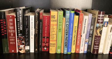 Photo of a bookshelf containing some of the books Amy Marcus read to understand the history of patient-led activism, the ethics of collaboration between patients and scientists, and the history of science in the modern era. Photo by Amy Marcus