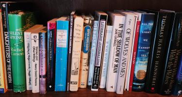 Rectangular photo of Marie Zhuikov’s office bookshelf with titles about wilderness and human nature. Photo credit Marie Zhuikov.