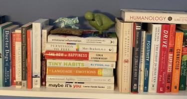 Rectangular photo of Stacey Colino’s office bookshelf with titles on dogs, happiness, and well-being. Photo credit Stacey Colino.