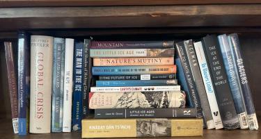 Rectangular photo of Lisa Baril’s office bookshelf with titles on archaeology, ice, glaciers, climate change, and writing a book proposal. Photo credit Lisa Baril.