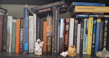 Rectangular photo of Christopher Pollon’s office bookshelf showing works on mining, capitalism, colonialism, sustainability, gold, oil, geology, wars, and various countries. Photo credit: Christopher Pollon.