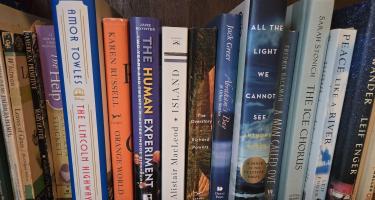 Rectangular photo of Marie Zhuikov’s office bookshelf showing works of poetry, fiction, and nonfiction on nature themes. These include Leaves of Grass, the Overstory, and The Human Experiment. Photo credit: Marie Zhuikov.