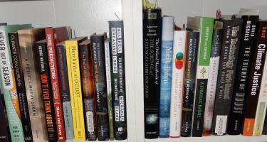 Rectangular photo of Dennis Meredith’s office bookshelf showing works on denial, morality, disasters, technology, politics, and climate change. Photo credit: Dennis Meredith.