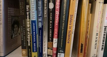 Rectangular photo of Ainissa Ramirez’s office bookshelf showing works on Black and White male and female scientists and their discoveries. Photo credit: Ainissa Ramirez.