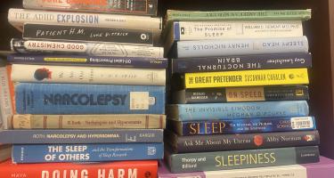 Rectangular photo of Quinn Eastman’s office bookshelf showing books on narcolepsy, sleep science, and the medical care system. Photo credit Quinn Eastman.