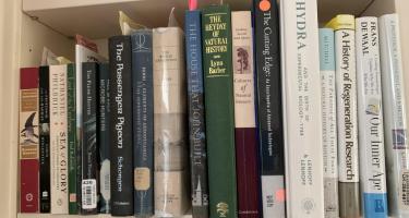 Rectangular photo of Ann Parson’s office book shelf showing works on explorers’ travels, natural history, and the development of technologies. Photo credit: Ann Parson.