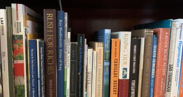 Rectangular photo of Erica Gies’ office bookshelf showing works on water and water-related topics including ecology, environmental legislation, rain, marshes, and rivers. Photo credit: Erica Gies.