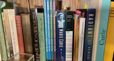 Rectangular photo of Liz Lee Heinecke’s office bookshelf showing works about and by women in science including Marie Curie and Rachel Carson. Photo credit: Liz Lee Heinecke.