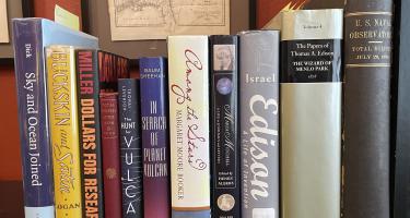 Rectangular photo of David Baron’s office bookshelf showing works on eclipses, starts, astronomy, Thomas Edison and the U.S. Naval Observatory’s record of the July 29, 1878 eclipse. Photo credit: David Baron.