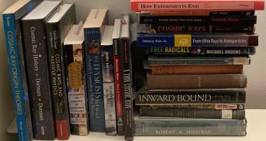 Rectangular photo of Mark Wolverton’s office bookshelf showing works by and about physicists Arthur Holly Compton and Robert Millikan, the subjects of his book Splinters of Infinity, along with books on cosmic rays, stars, astronomy, and physics. Photo credit: Mark Wolverton.