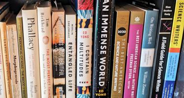 Rectangular photo of a closeup of books on a shelf, spanning titles on science writing. Photo by Danna Staaf
