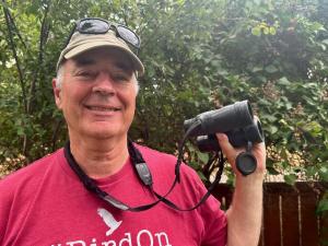 Portrait photo of Sneed B. Collard III outdoors holding his birding binoculars. 