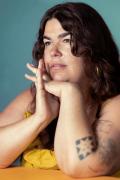 Portrait photo of Elizabeth Endicott posing with elbows on a table, hands to chin, looking away from the camera. Photo credit Aurora Adams.