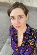 Portrait photo of Kat Eschner wearing a blouse with tropical foliage motifs, looking up at the camera.