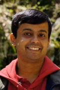 Portrait photo of Sandeep Ravindran smiling and wearing a jacket outdoors before greenery