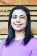 Portrait photo of Aparna Vidyasagar, who identifies as a South Asian female, smiling and posing outdoors in front of a wooden screen.